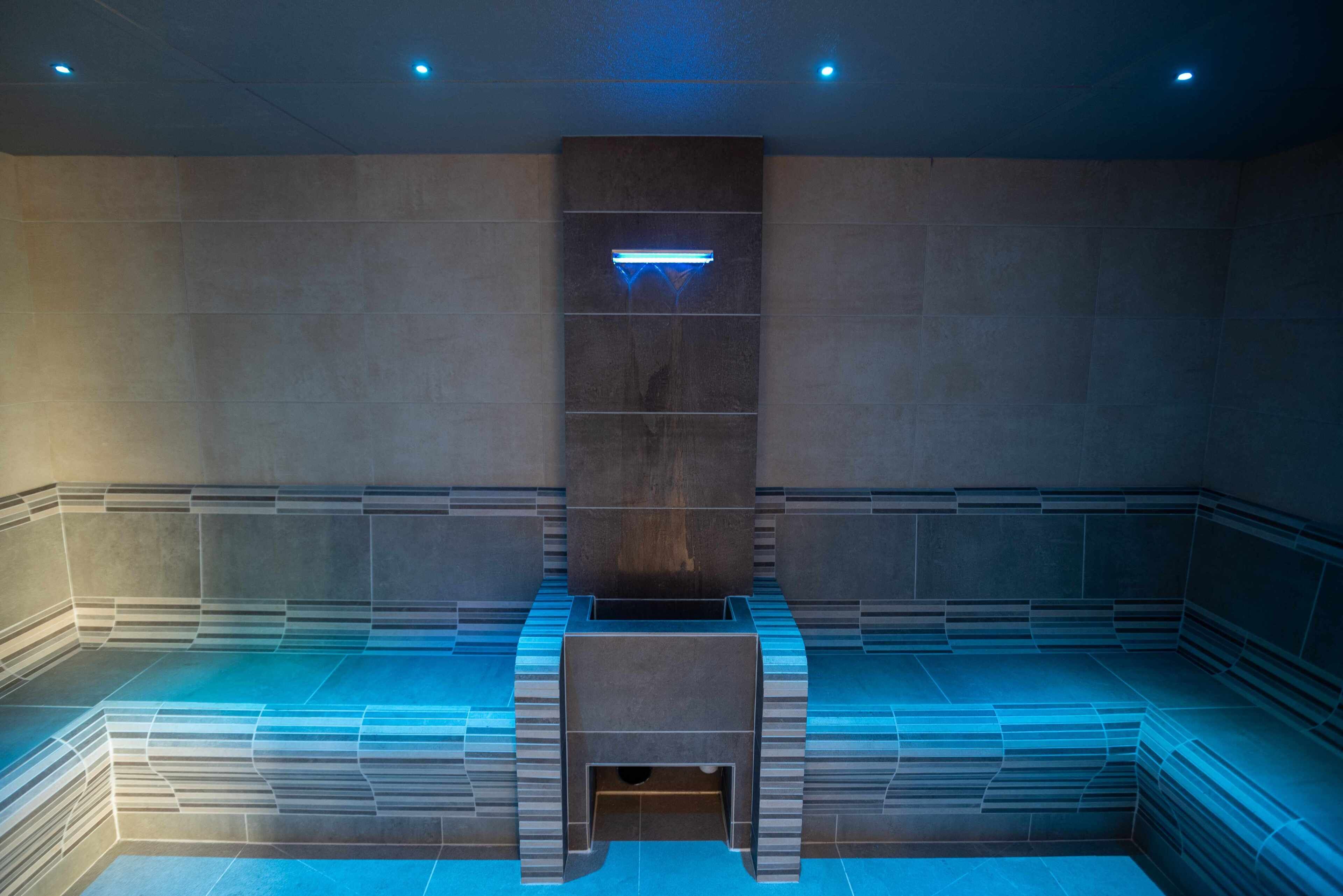 A modern, minimalist sauna with a geometric design, featuring a central bench and a light fixture above.