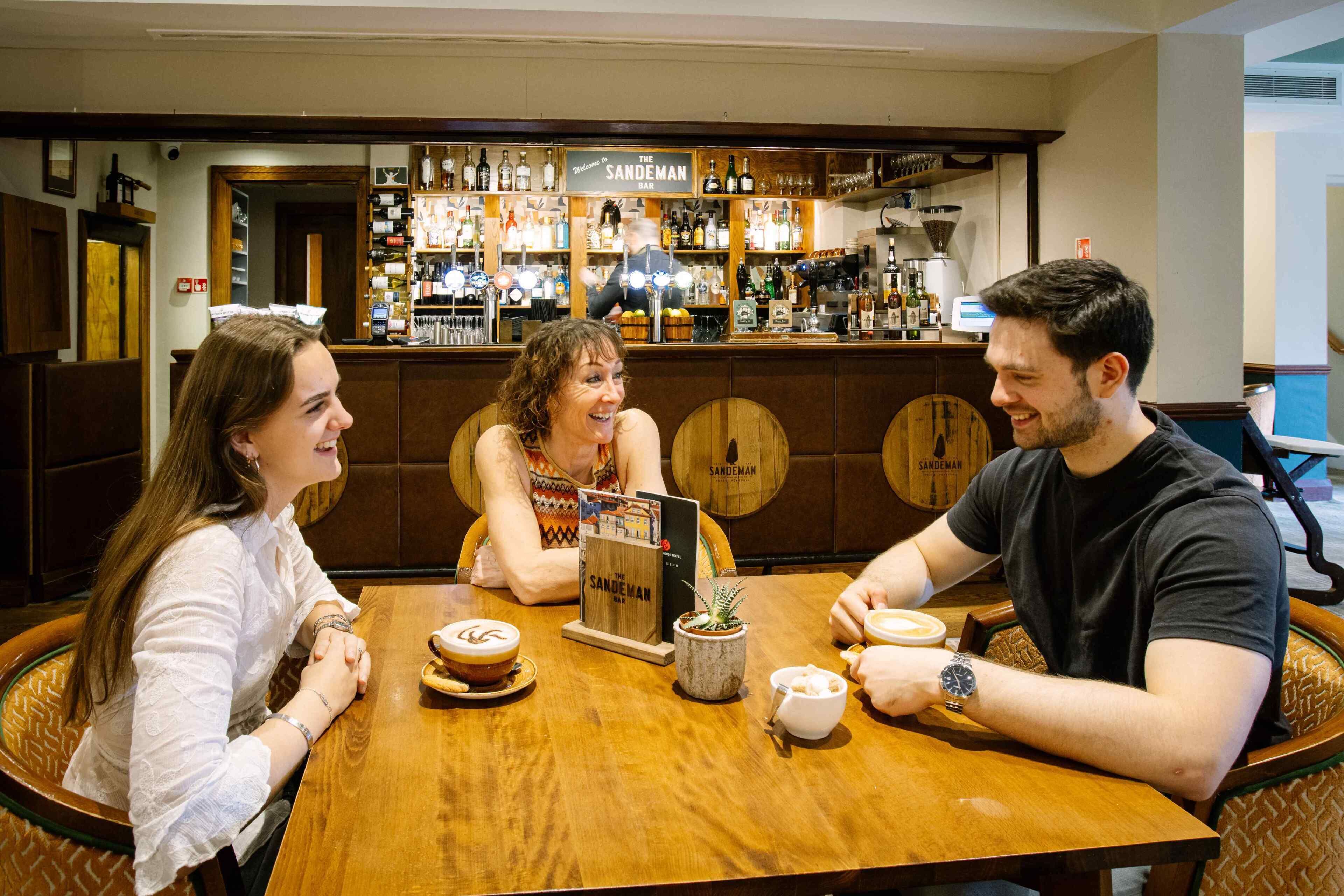 Una zona de bar con mostrador de madera, estantes llenos de botellas y un atril para el menú.