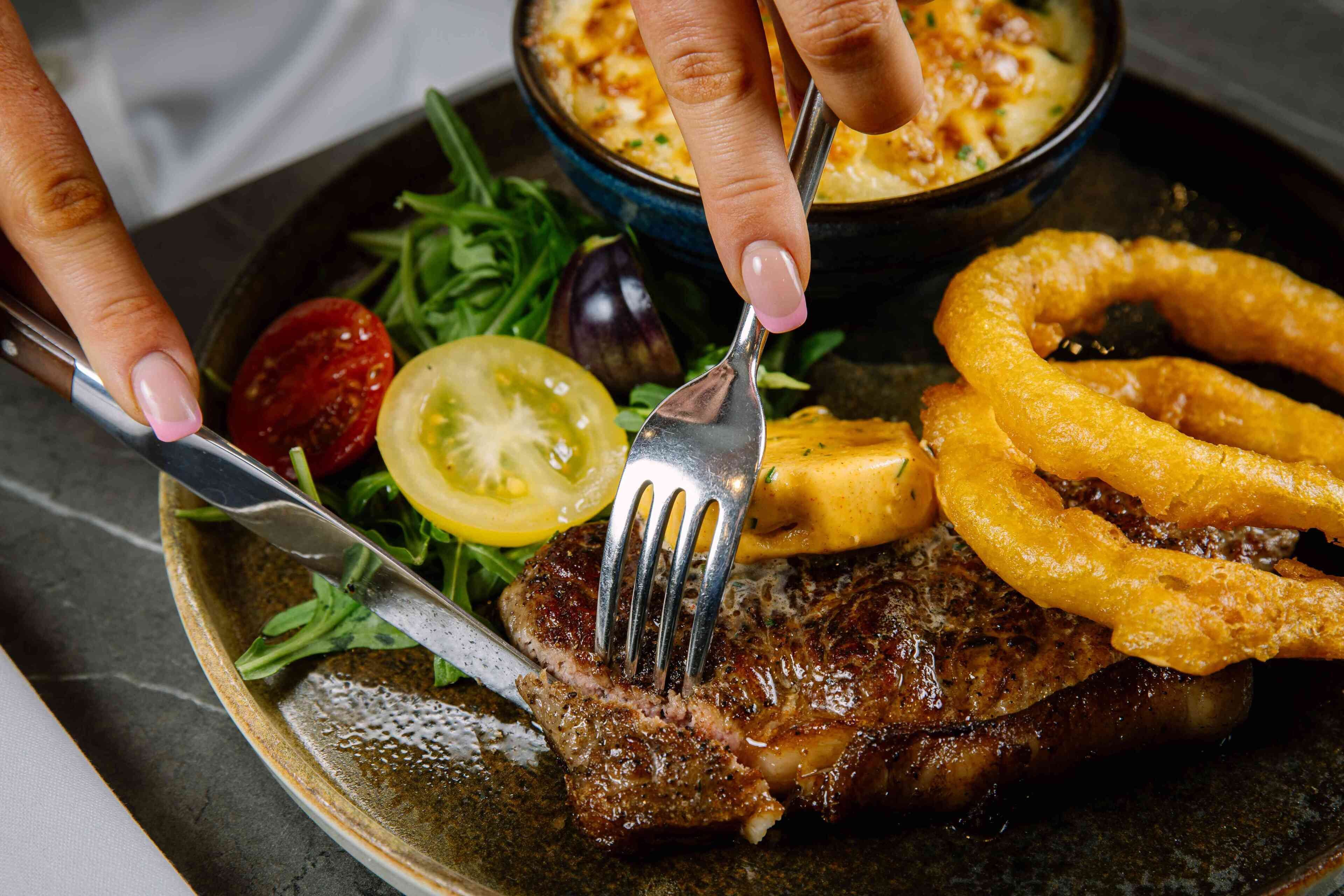 A plate with a grilled steak, onion rings, a slice of tomato, and a side salad.