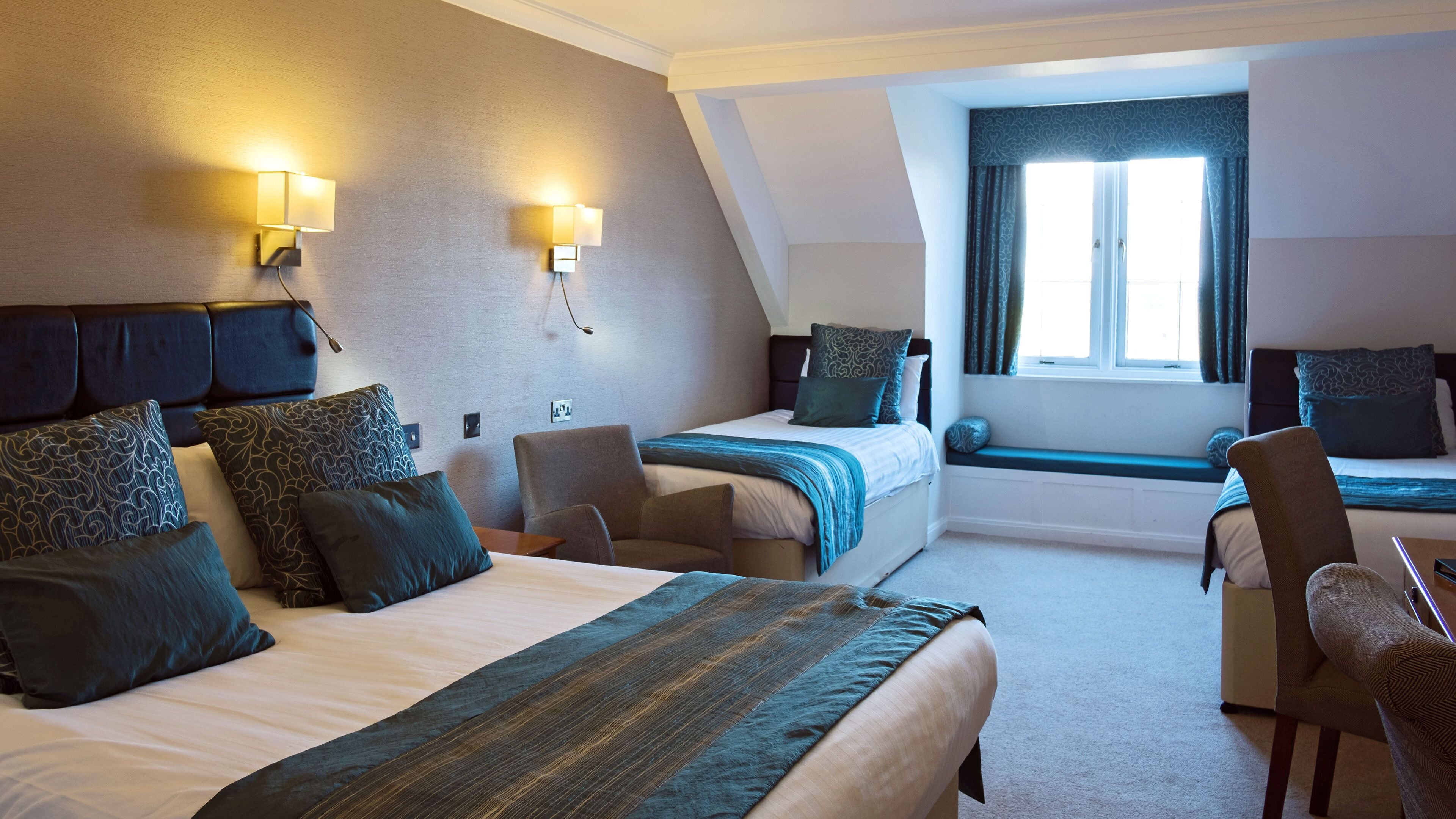 A hotel room with a large bed, a smaller bed, a seating area, and a window with curtains.