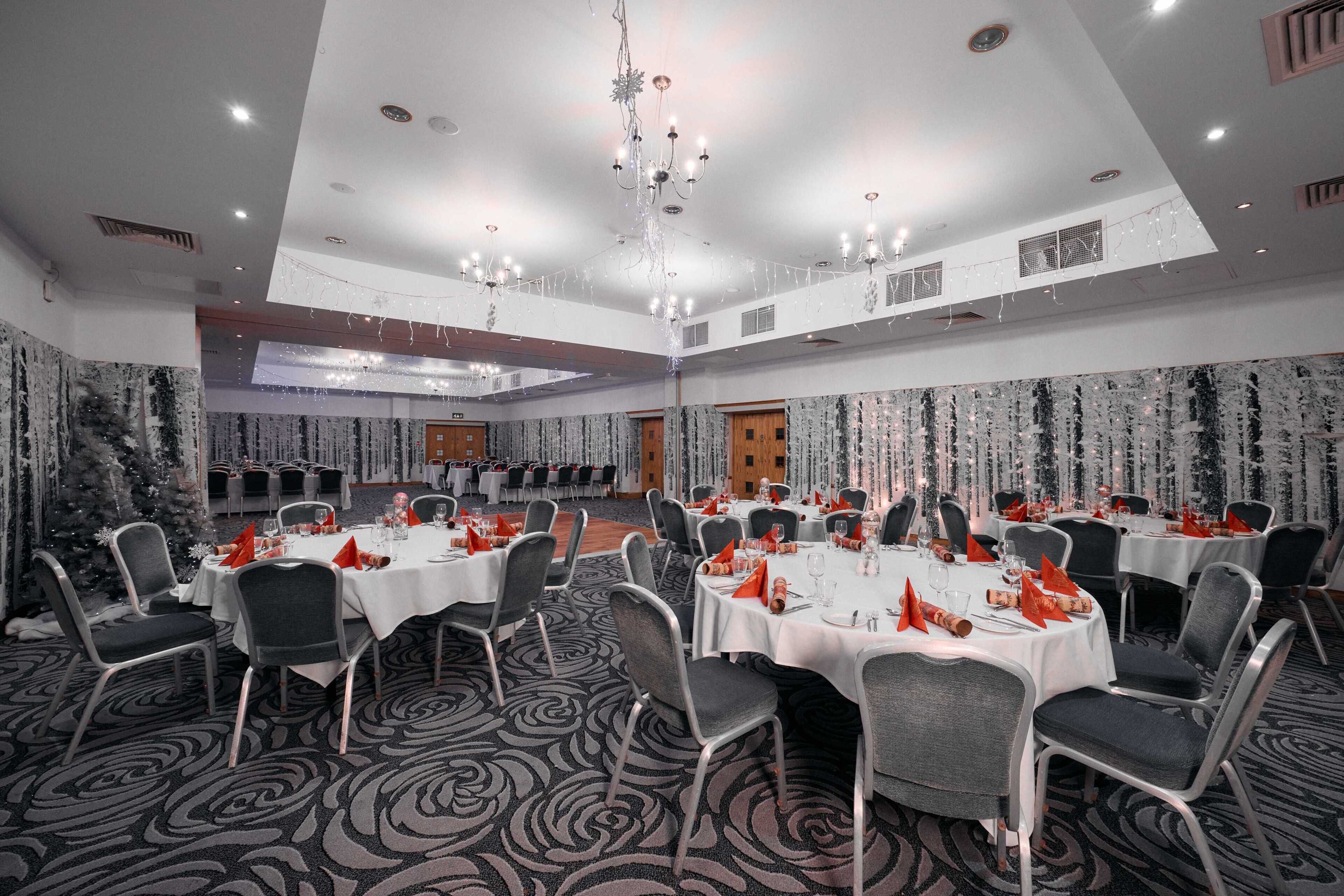 A banquet hall with round tables, chairs, and a chandelier.