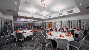 A banquet hall with round tables, chairs, and a chandelier.
