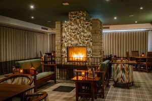 Un rincón lounge acogedor con chimenea de piedra, asientos cómodos y alfombra estampada.