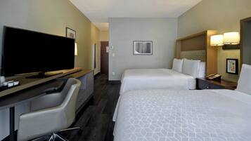 Habitación de hotel con dos camas, un escritorio, un televisor de pantalla plana, una silla y una mesita de noche con lámparas.