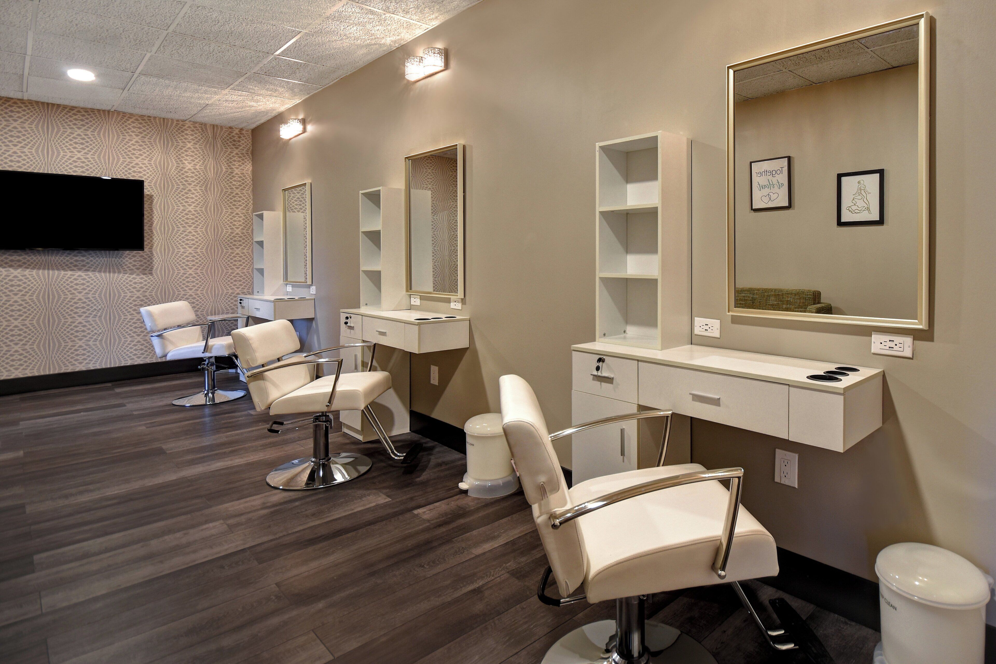 A salon with three chairs, mirrors, and a flat-screen TV on the wall.