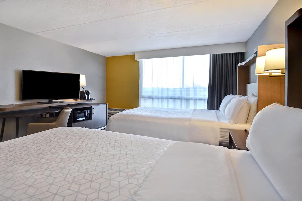 A hotel room with two beds, a desk, a television, and a window with curtains.