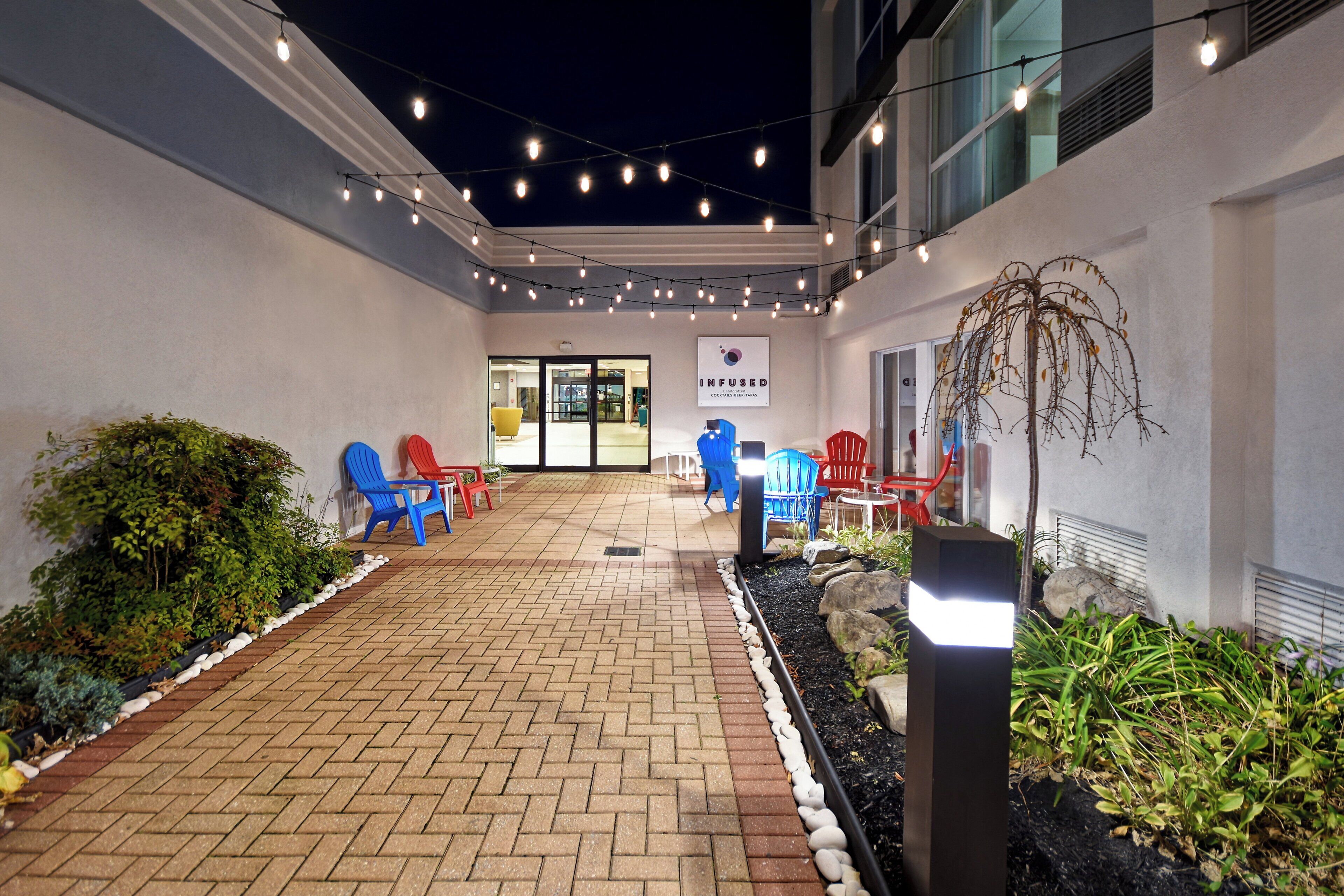 An outdoor patio area with brick flooring, outdoor seating with blue and red chairs, and string lights.