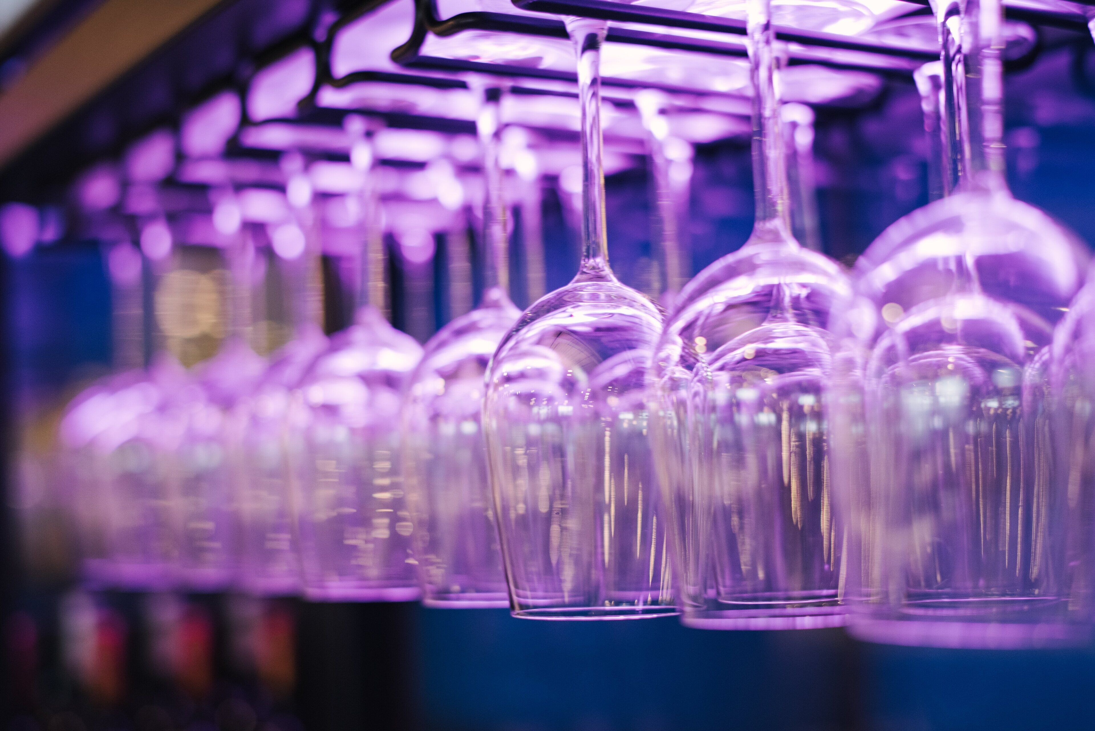 A row of empty wine glasses hanging from a rack.
