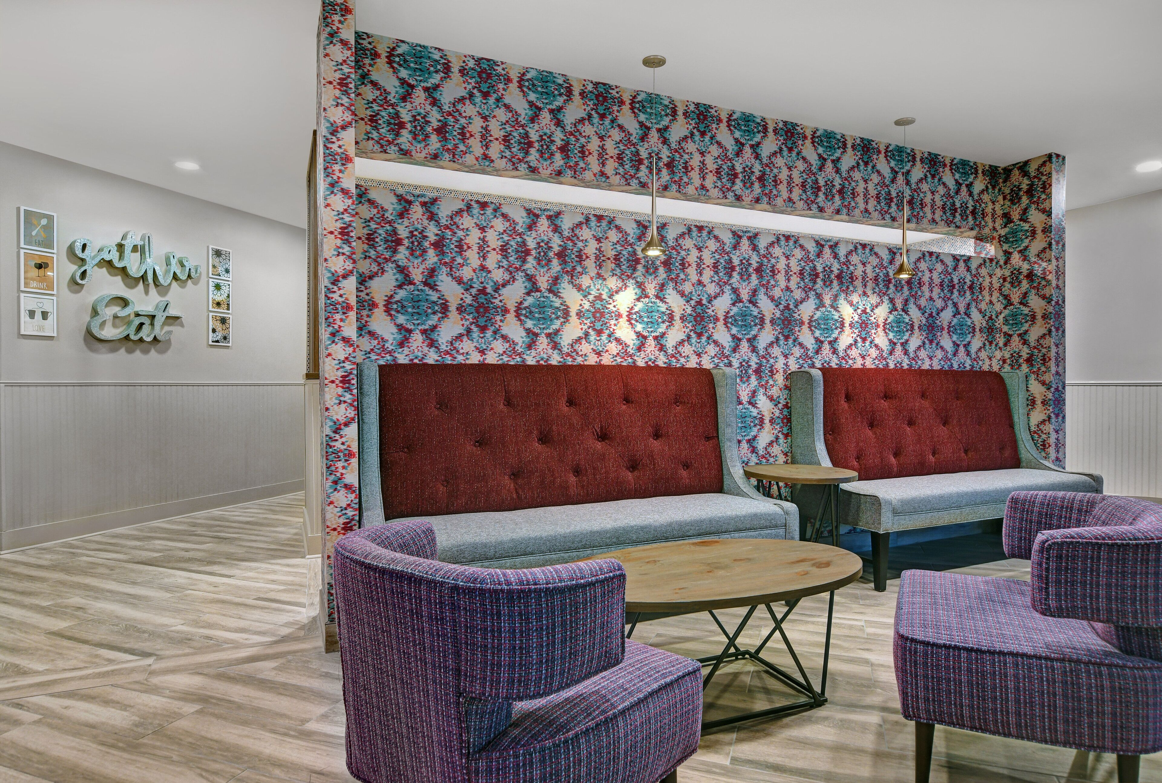 Un vestíbulo con un sofá rojo con capitonado, dos sillones morados, una mesa de centro redonda de madera y una pared con estampado.