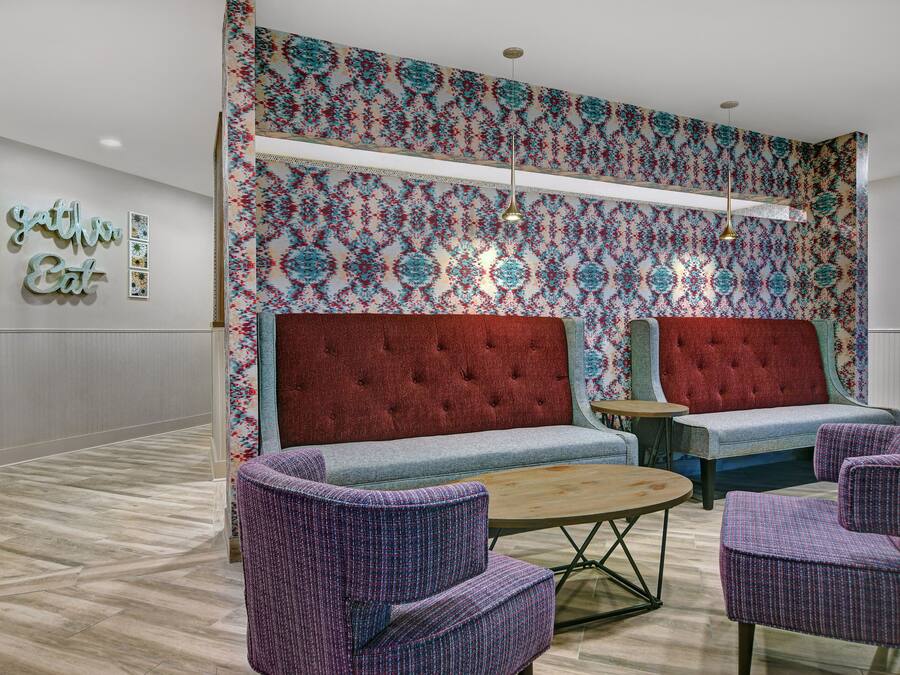 Un vestíbulo con un sofá rojo con capitonado, dos sillones morados, una mesa de centro redonda de madera y una pared con estampado.