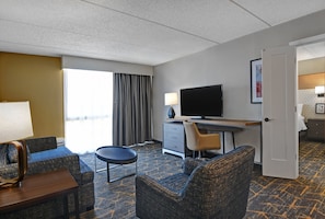Quarto de hotel com uma mesa, duas cadeiras, televisão, luminária e uma cama.