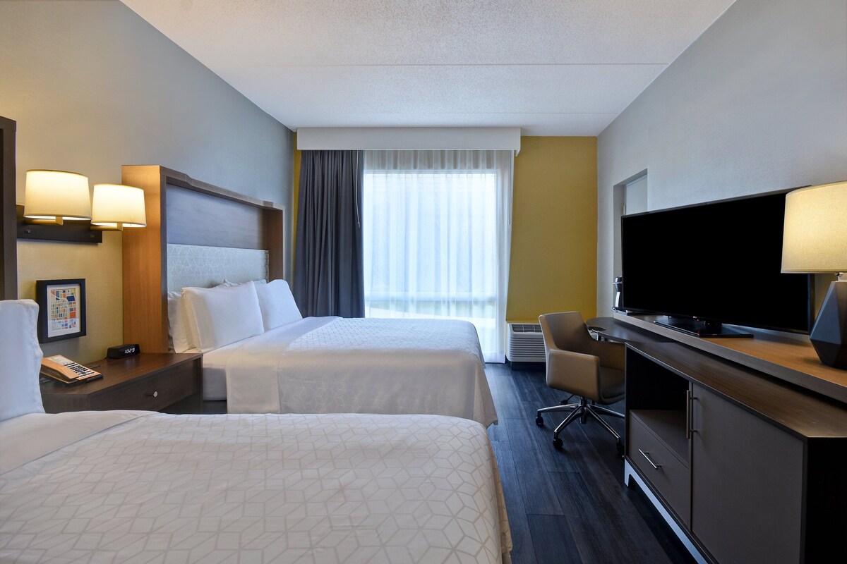 A hotel room with two beds, a TV, a desk, and a chair.