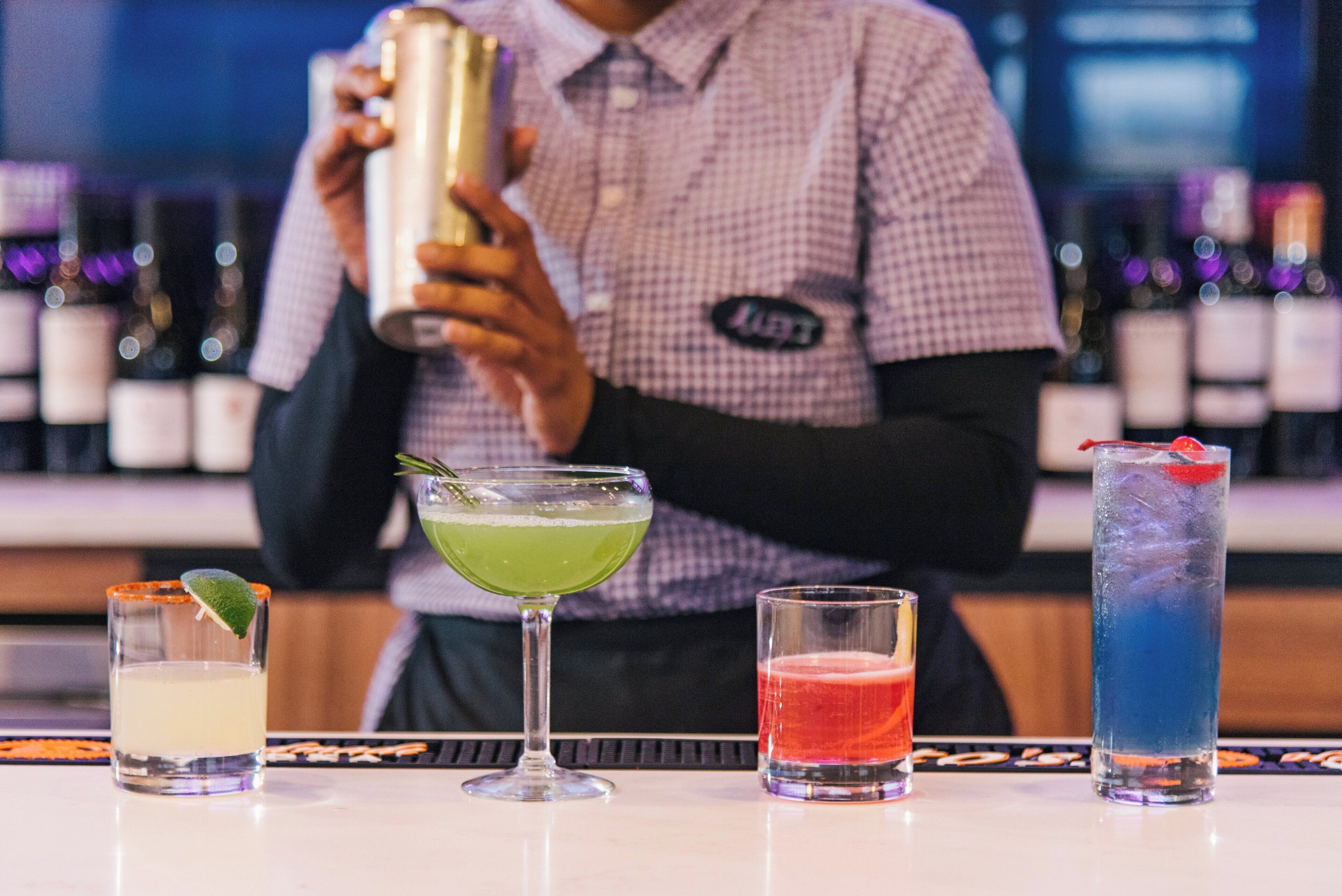 Un barman prépare des boissons derrière un comptoir, avec différents cocktails exposés devant lui.
