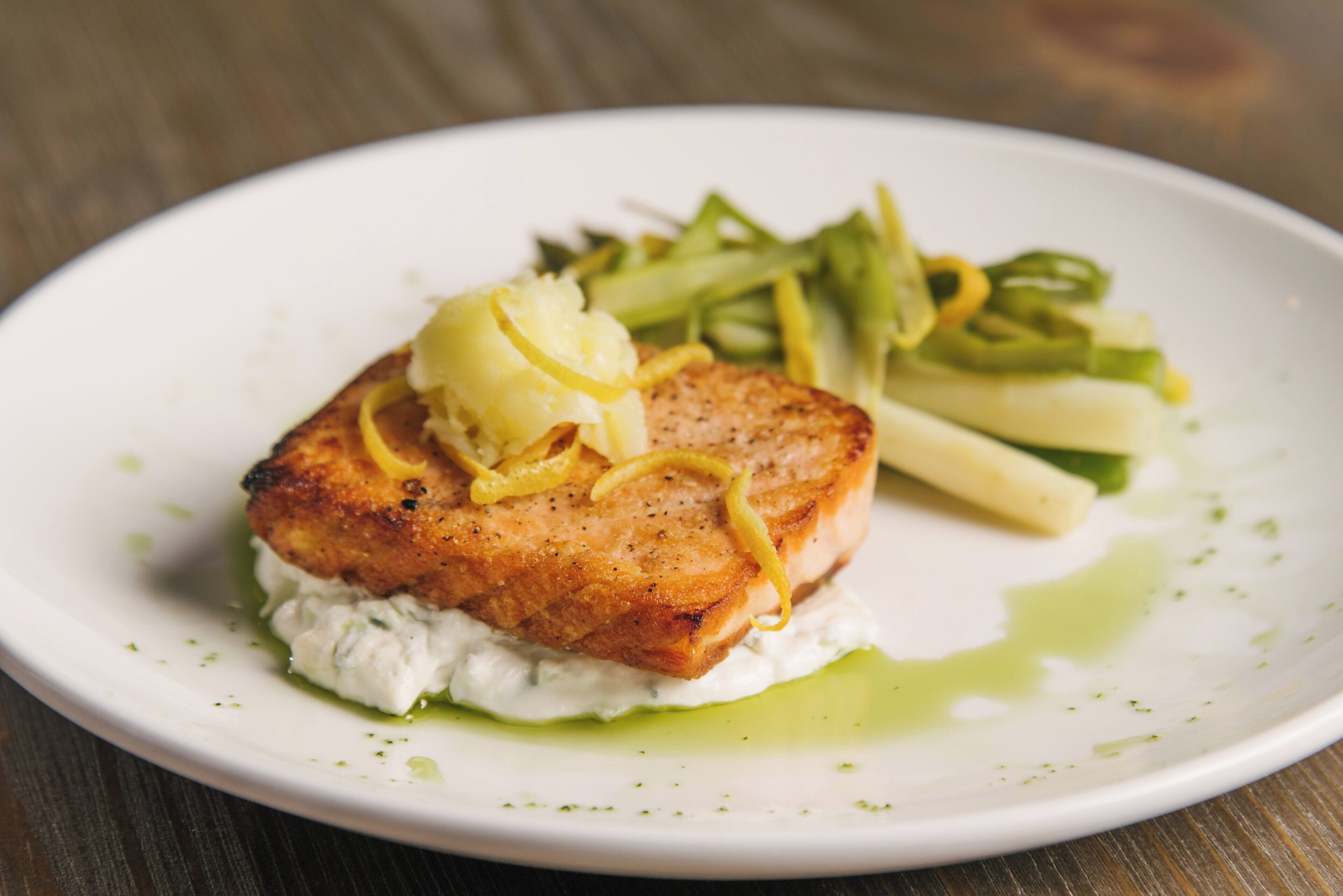 Un plato blanco con un trozo de pescado a la parrilla, rodajas de limón y salsa verde.