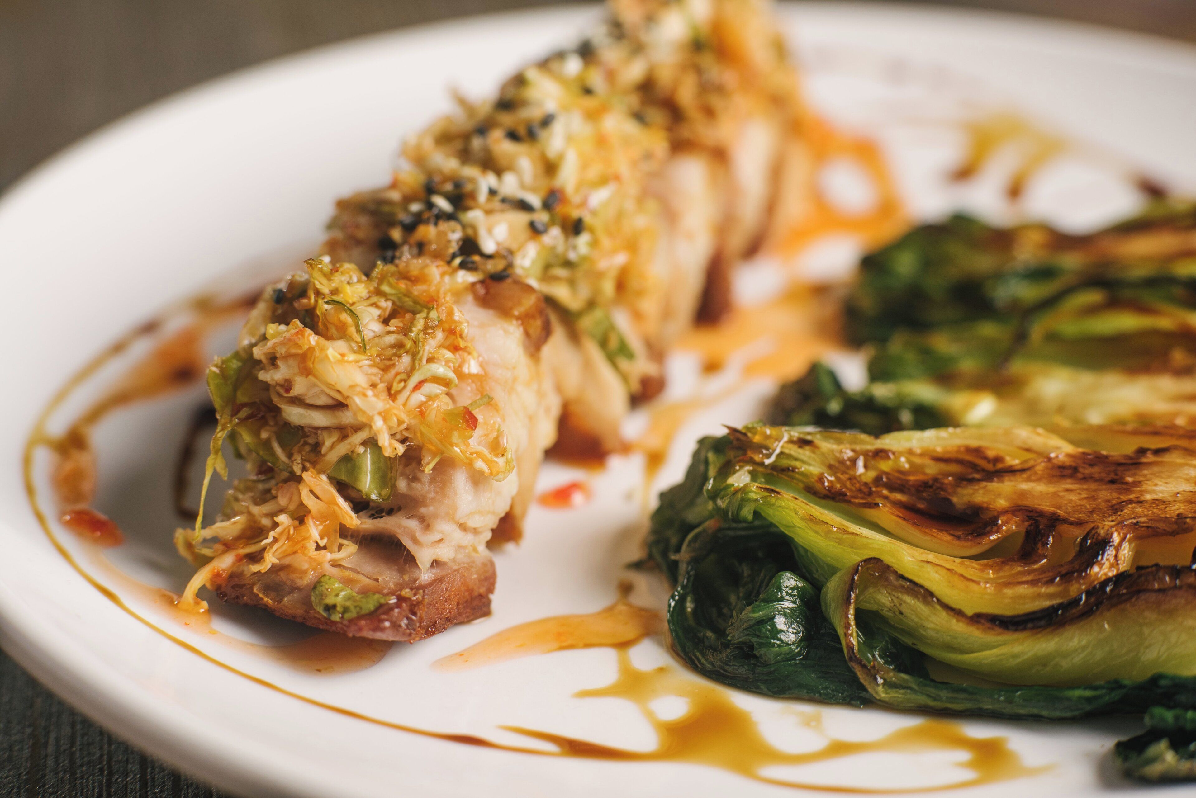 A plate with a stuffed chicken breast, roasted Brussels sprouts, and a drizzle of sauce.