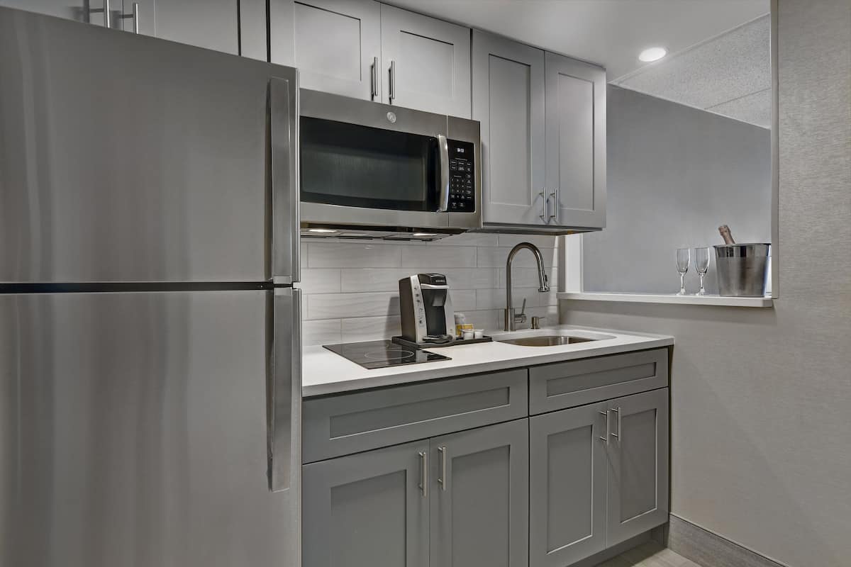 A modern kitchen with stainless steel appliances, grey cabinets, and a white countertop.