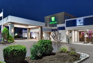 Un hotel Holiday Inn con fachada moderna, entrada bien iluminada y jardines ajardinados.