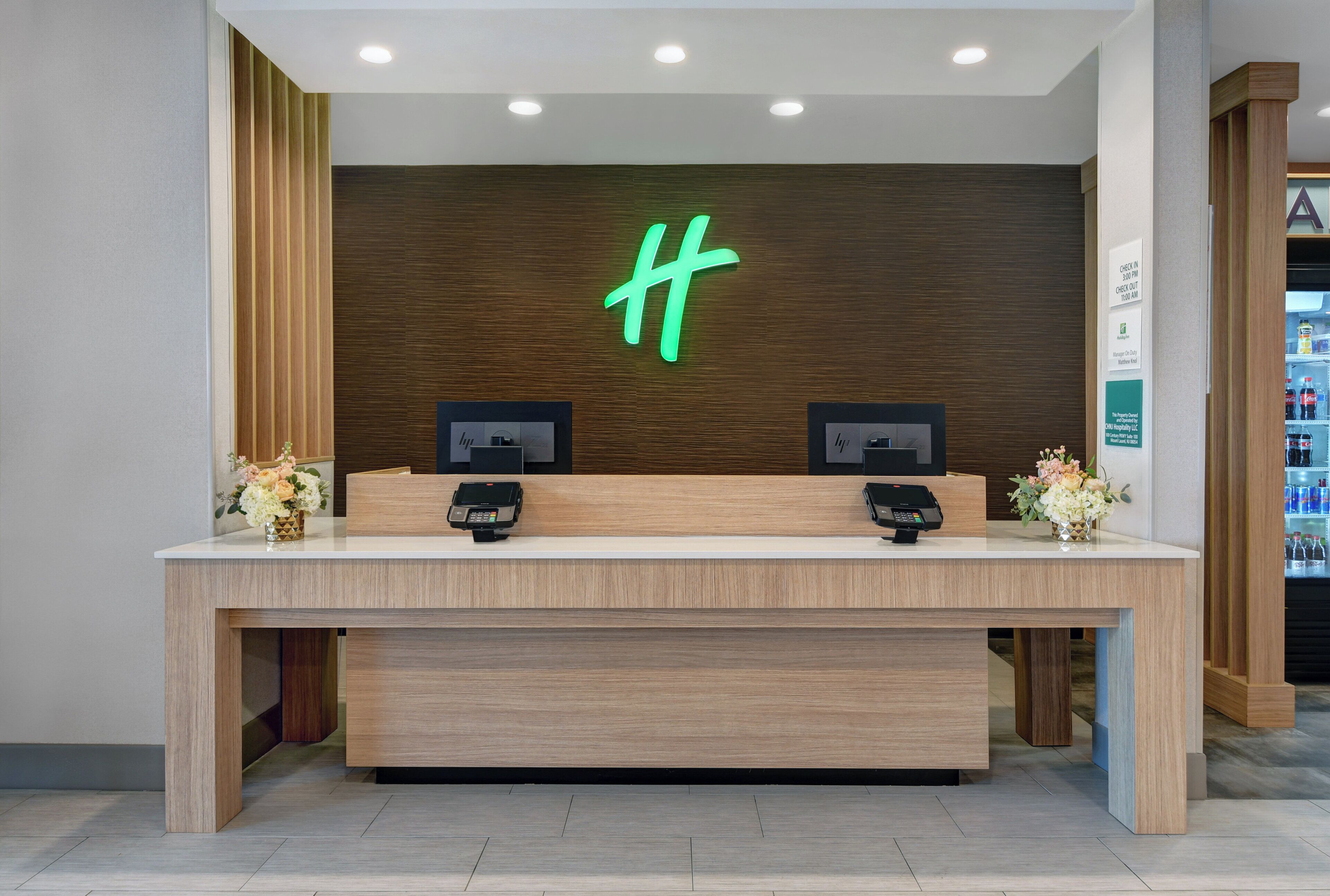 A reception desk with two card readers, a neon 'H' sign, and a refrigerator stocked with beverages.