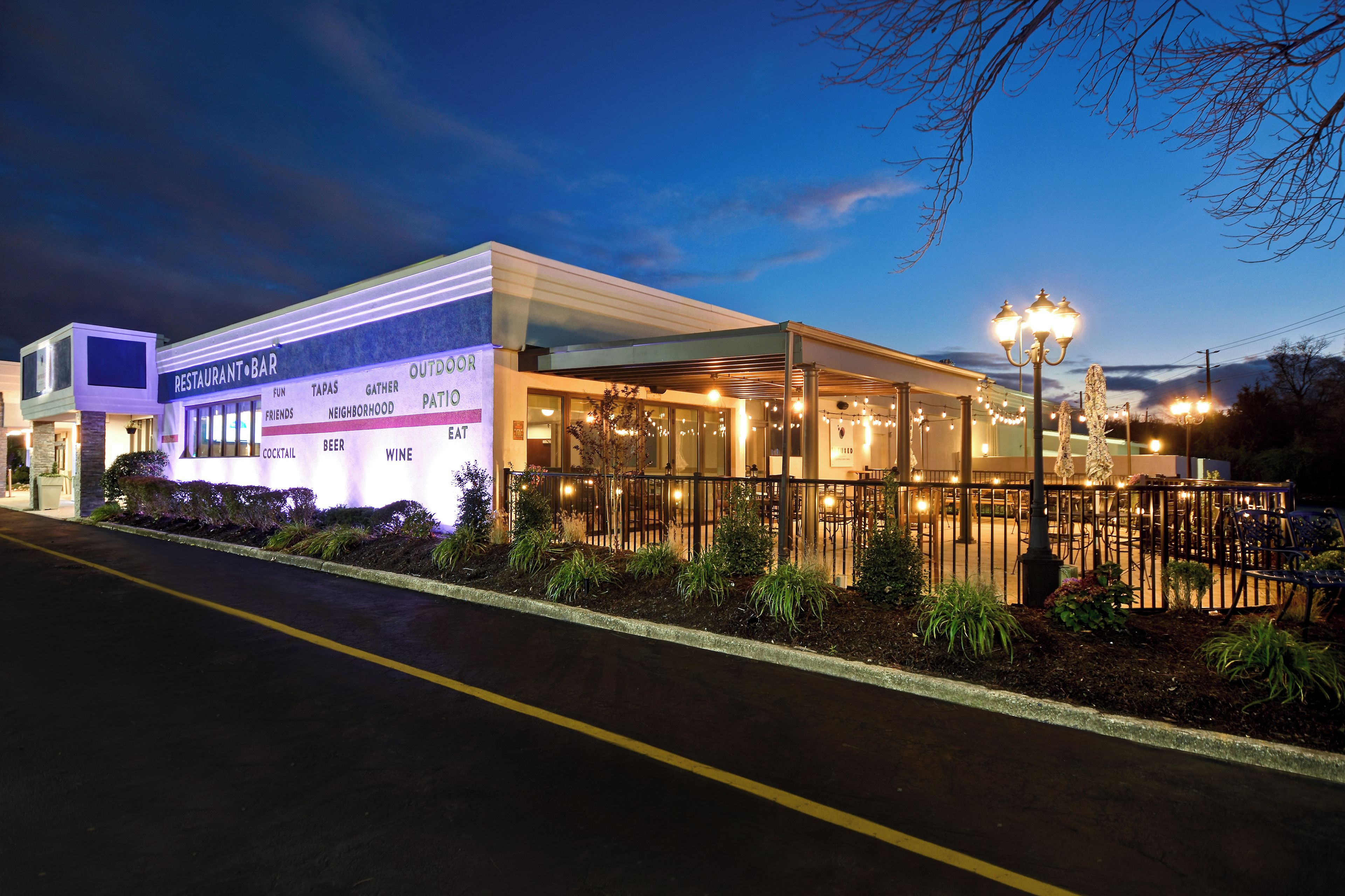 A restaurant with outdoor seating, a patio area, and a sign indicating it offers beer, cocktails, and wine.