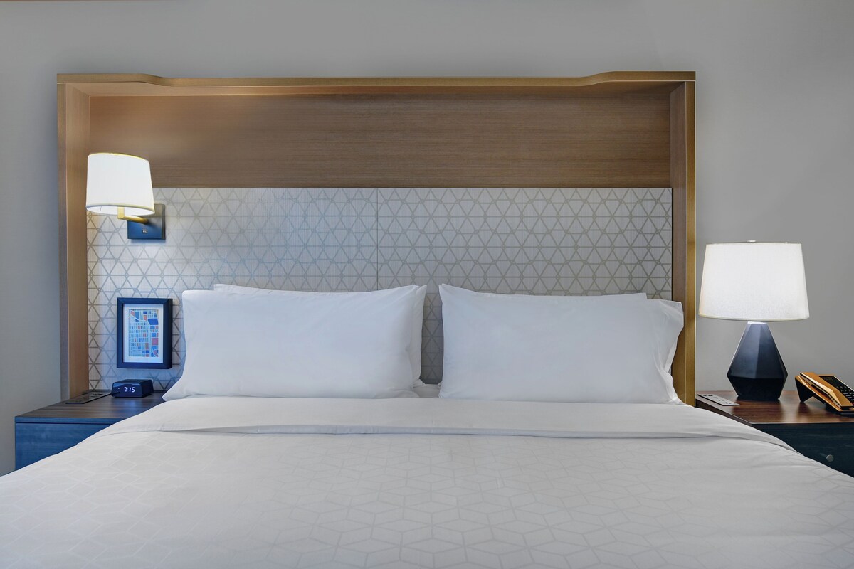 A hotel room with a large bed, two bedside tables, a wall clock, and two wall-mounted lamps.