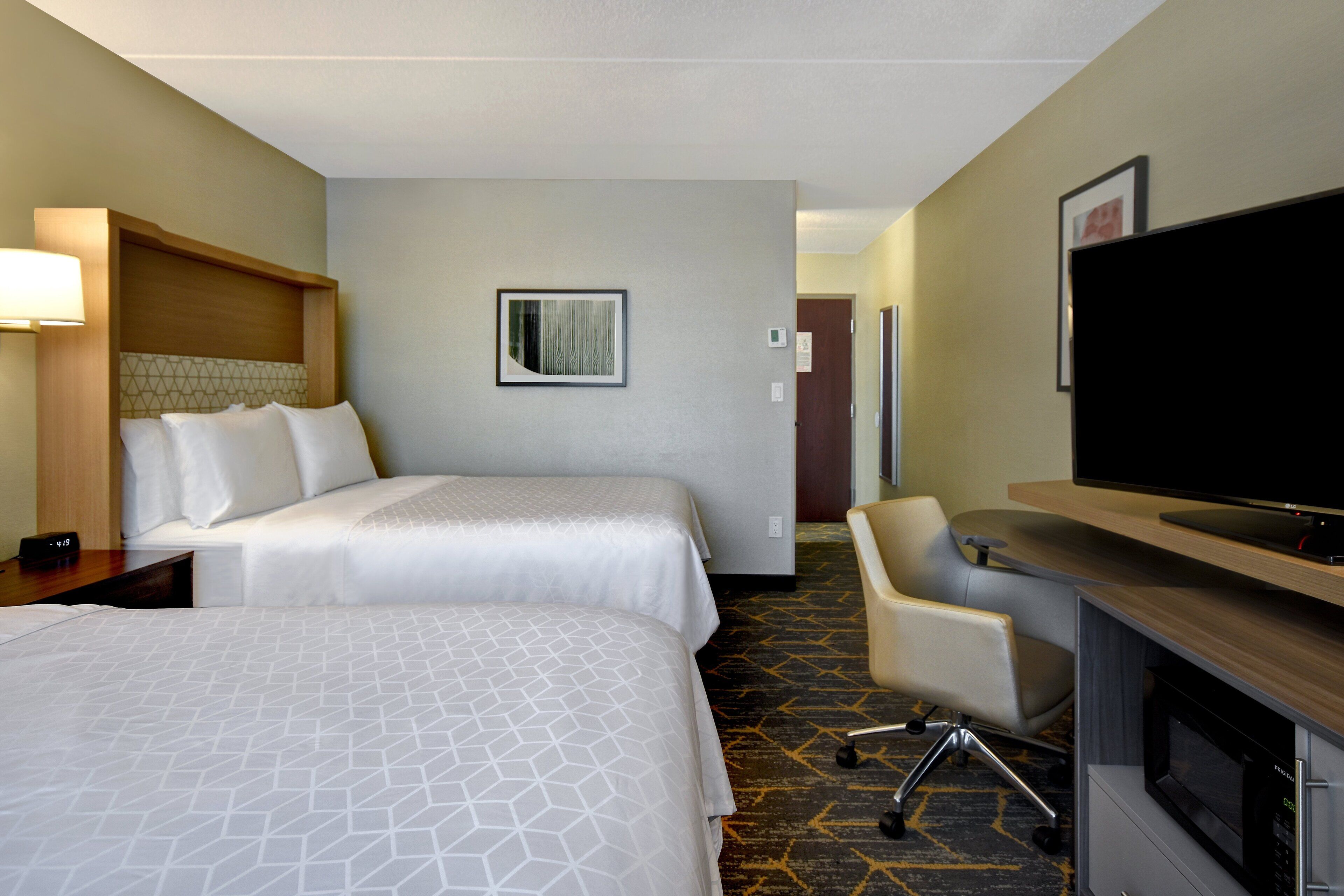 Quarto de hotel com duas camas, uma escrivaninha com televisão de tela plana, uma cadeira e um micro-ondas.
