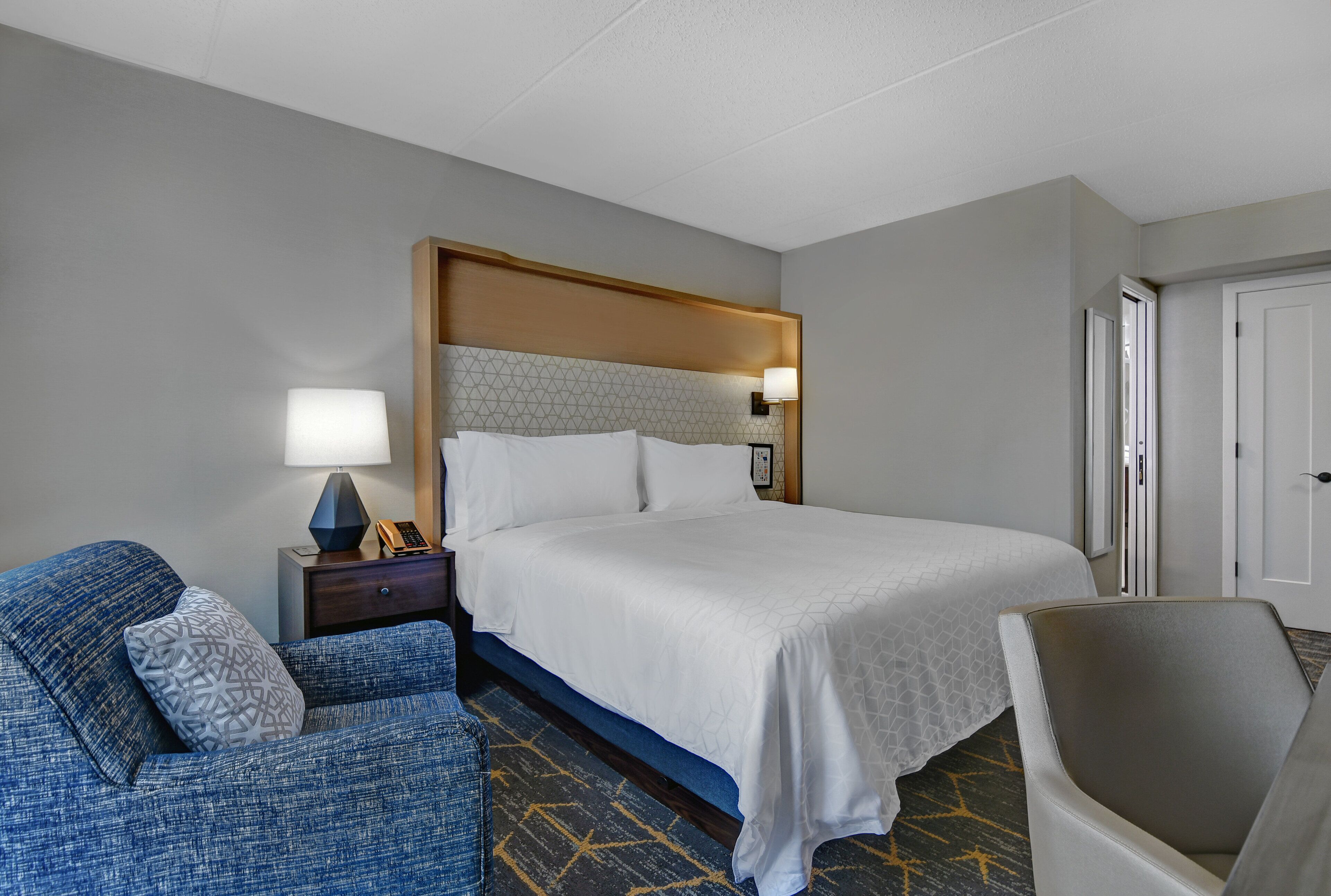 Une chambre d’hôtel avec un grand lit, un bureau avec une lampe, une chaise et une porte.