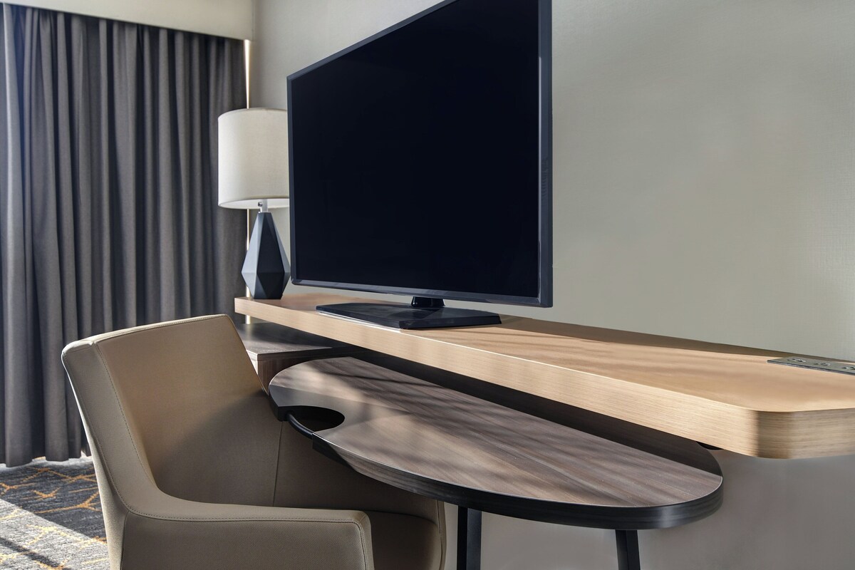 A hotel room with a desk, a flat-screen TV, a lamp, and a chair.