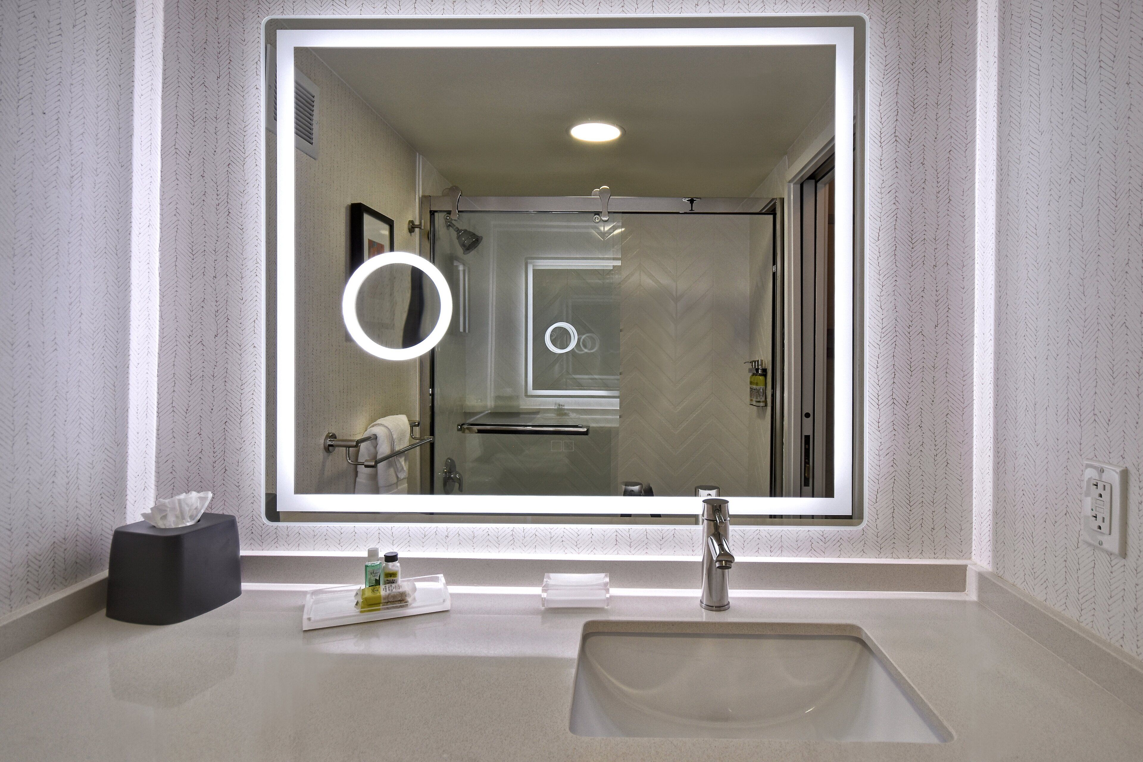 Un baño moderno con un espejo grande, un lavamanos y una ducha.