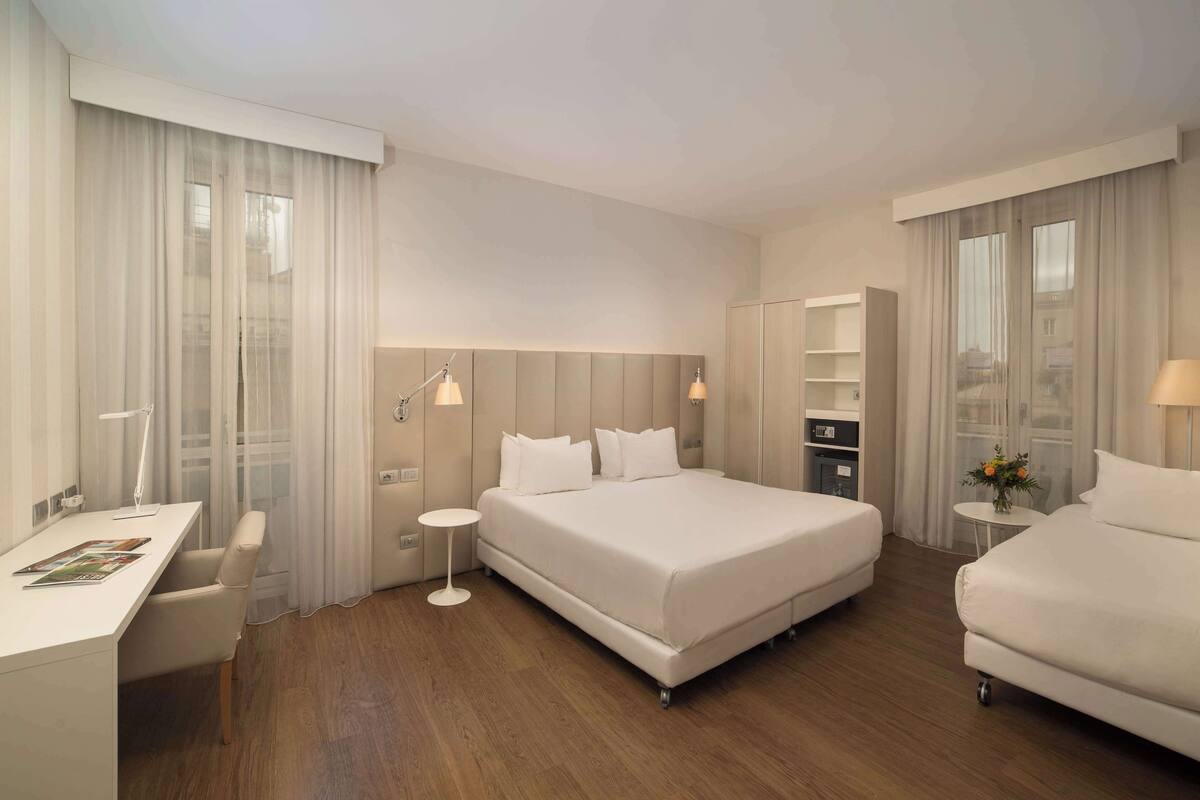 A modern hotel room with a large bed, a desk, and a small table.