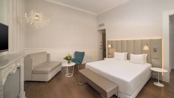 Ein modernes Hotelzimmer mit einem großen Bett, einer Couch, einem kleinen Tisch mit Blumen, einer Bank und einem Fernseher.