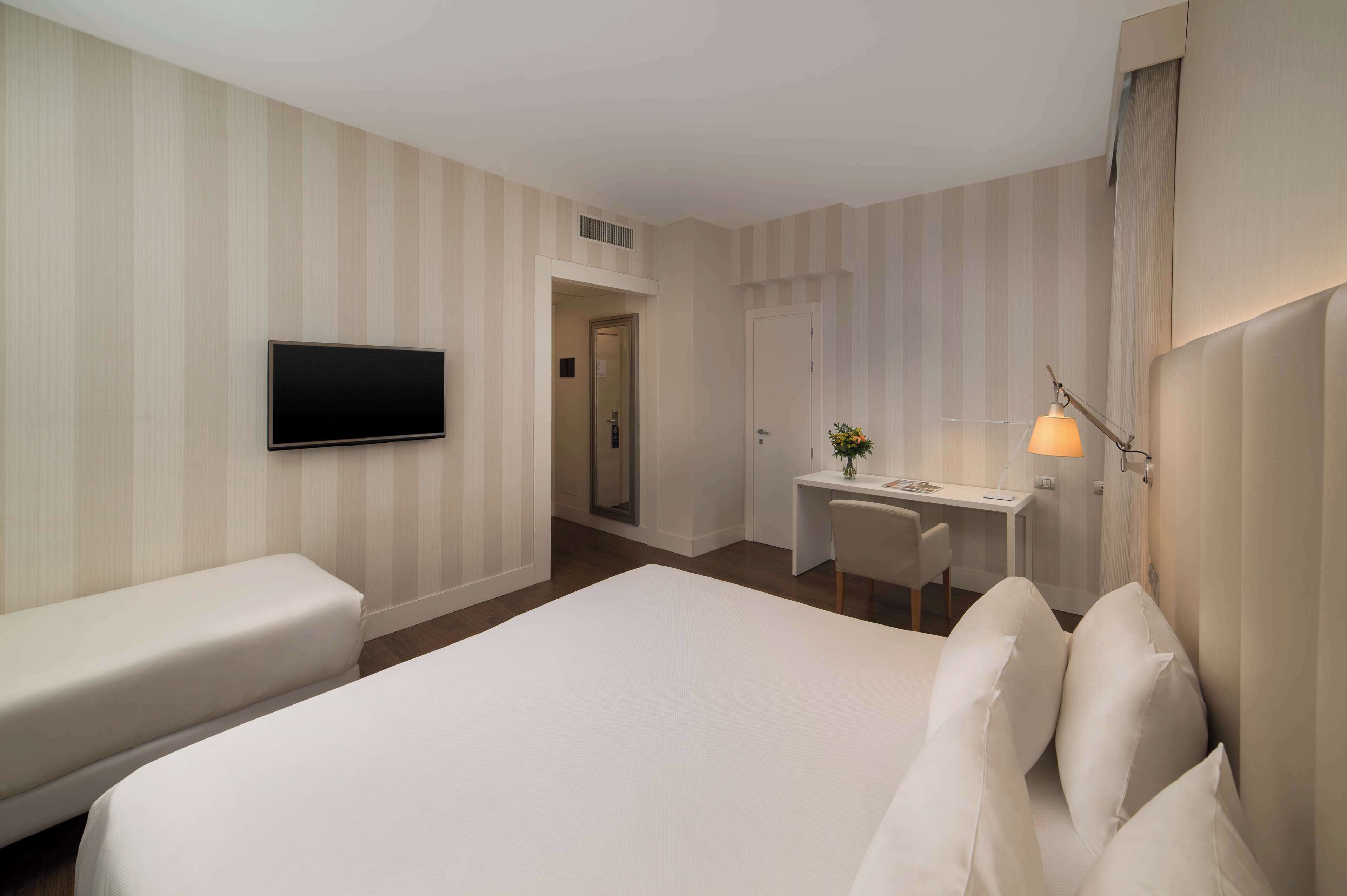 Habitación de hotel con una cama grande, un escritorio con lámpara, televisión y puerta que da a un baño.
