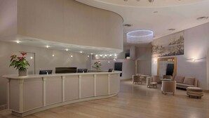 A modern reception area with a curved counter, seating, and a large painting on the wall. - NH Genova Centro (Genoa)