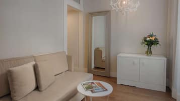 Una sala de estar moderna con un sofá color beige, una mesita de noche blanca con revistas, un armario blanco y un espejo que refleja una silla.