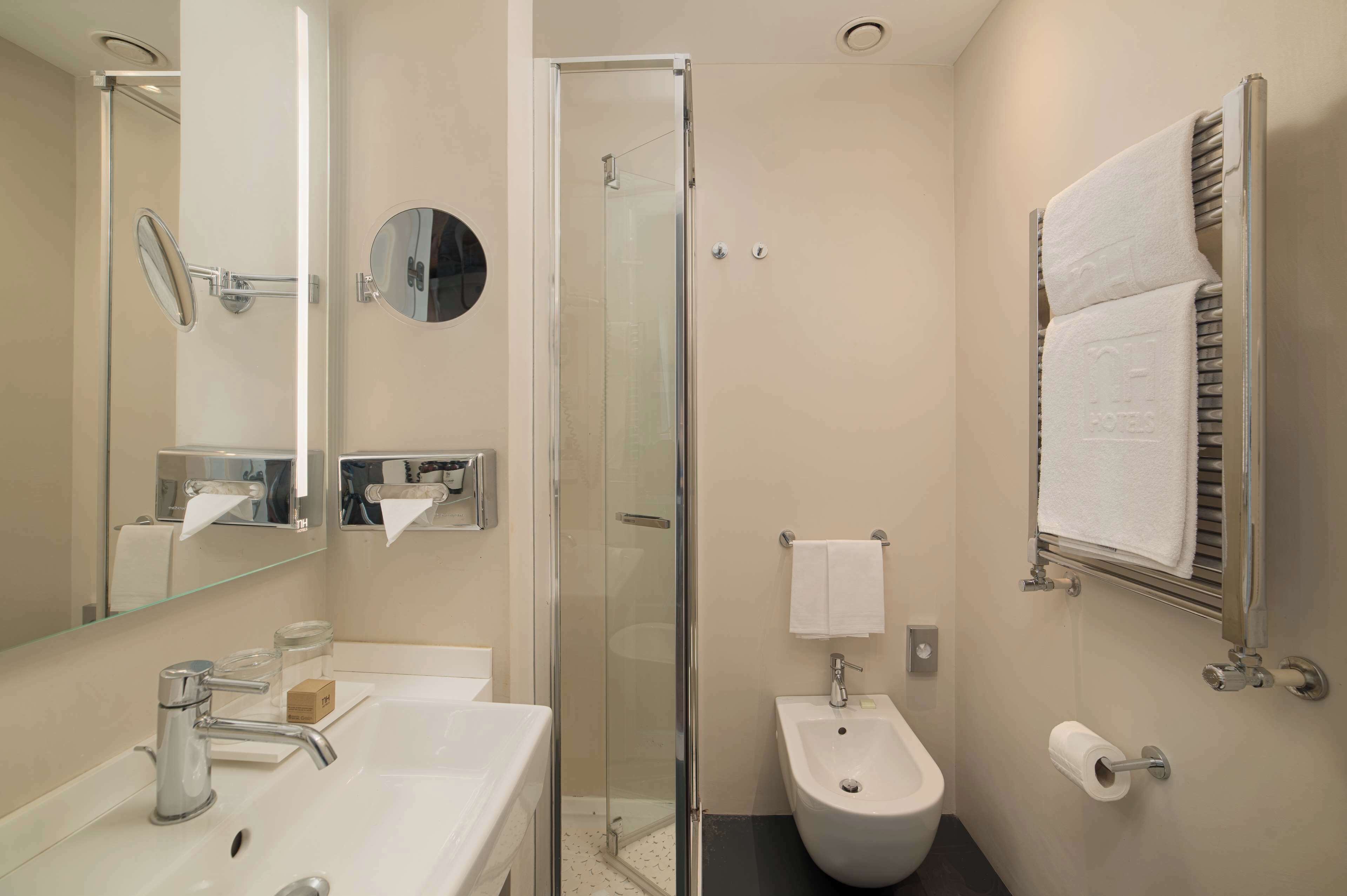A modern bathroom with a glass-enclosed shower, a white sink with a mirror, a bidet, and a towel rack.