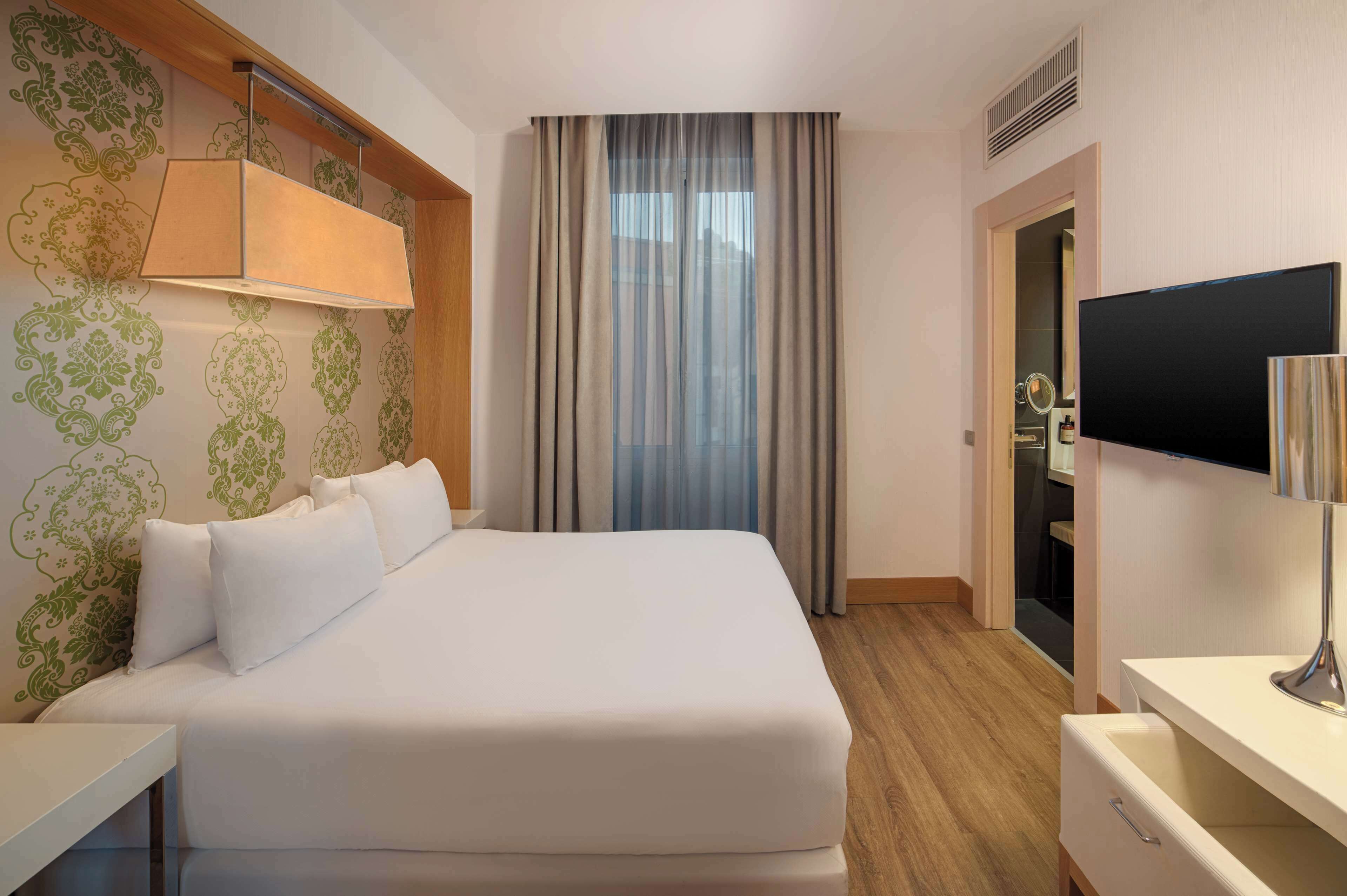 Ein Hotelzimmer mit einem großen Bett, einem Schreibtisch, einem Fernseher und einem Kleiderschrank.