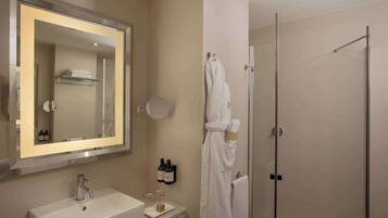 Un baño con un espejo grande, un lavamanos, una cabina de ducha de vidrio y un perchero para toallas.