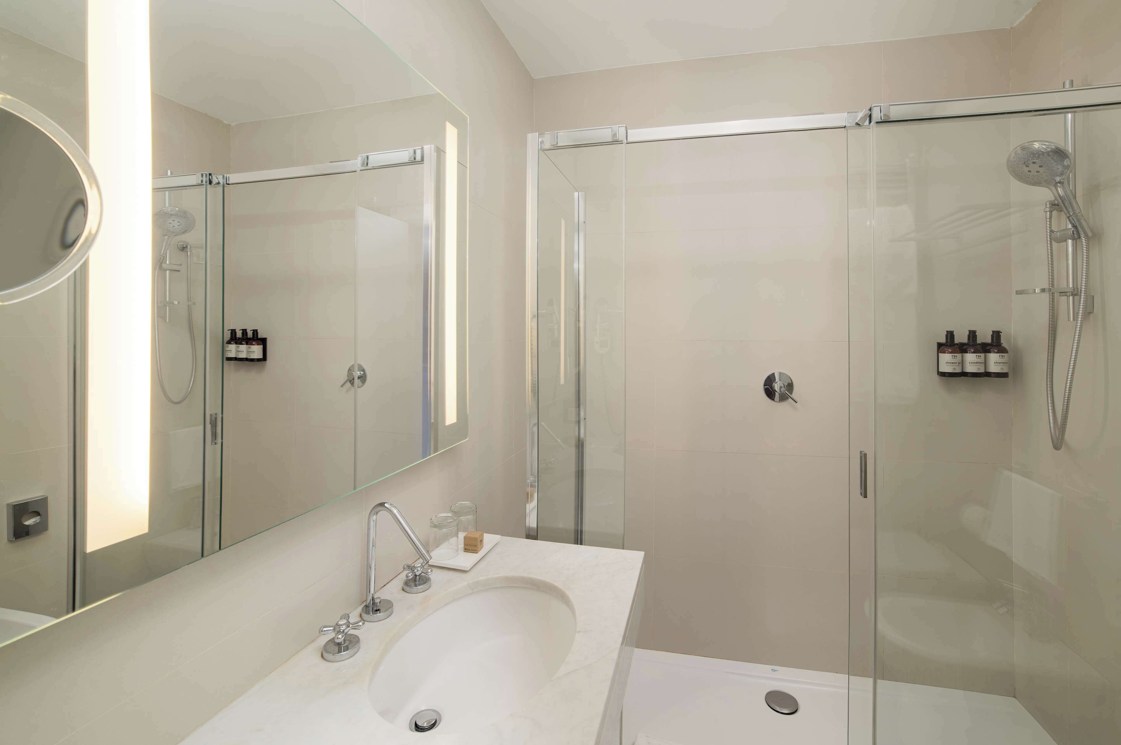 A modern bathroom with a glass-enclosed shower, a large mirror, and a white sink.