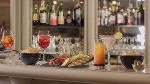 A bar area with a variety of drinks and snacks, including a martini, a cocktail, and a plate of appetizers. - NH Genova Centro (Genoa)