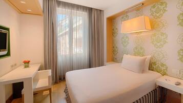 Une chambre d’hôtel avec un lit, un bureau, une chaise, une lampe et un téléviseur.