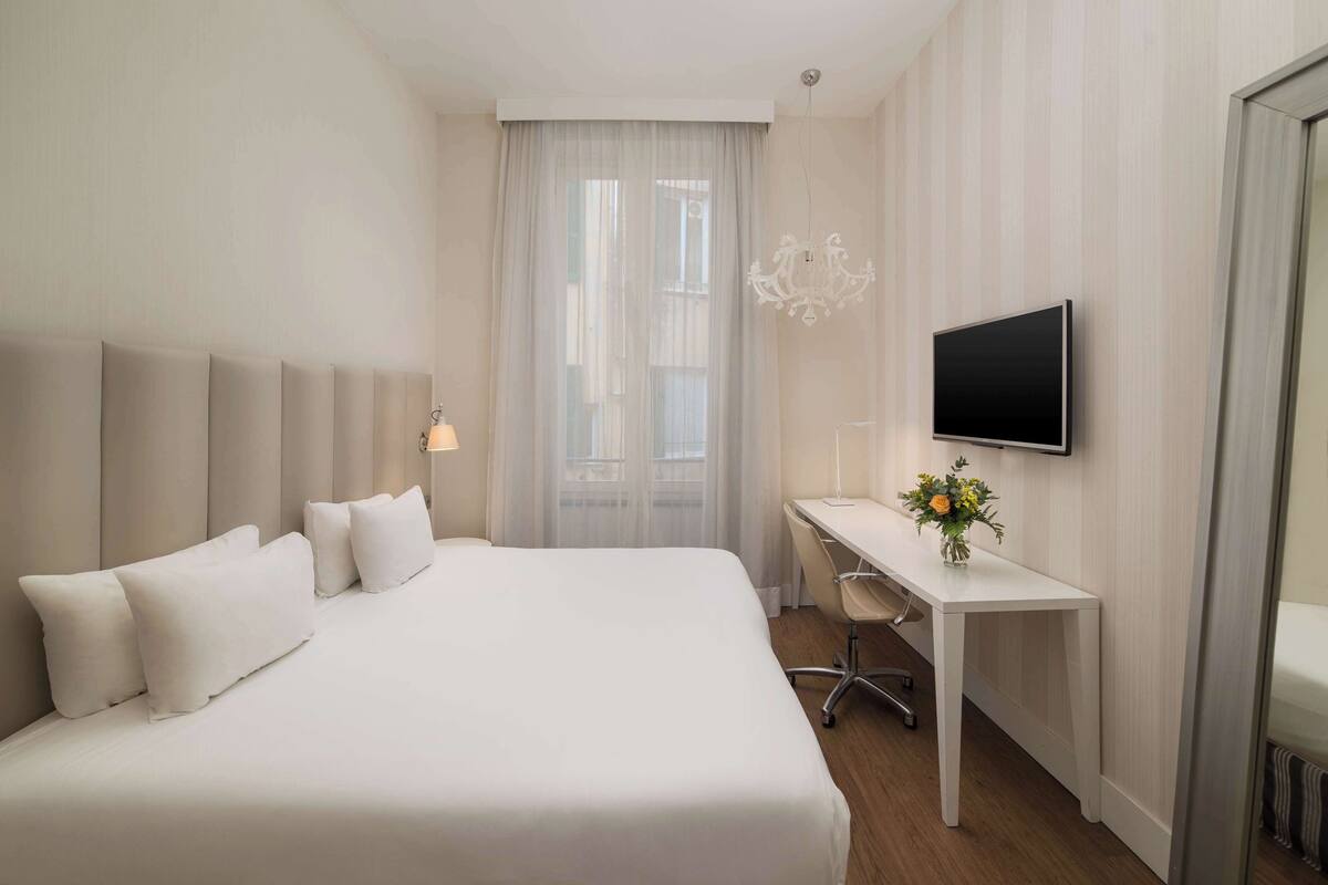 A hotel room with a large bed, a desk, a chair, a television, and a window with curtains.