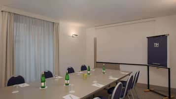 Ein Konferenzraum mit langem Tisch, Stühlen, einer Projektionsleinwand und einem Fenster mit Vorhängen.