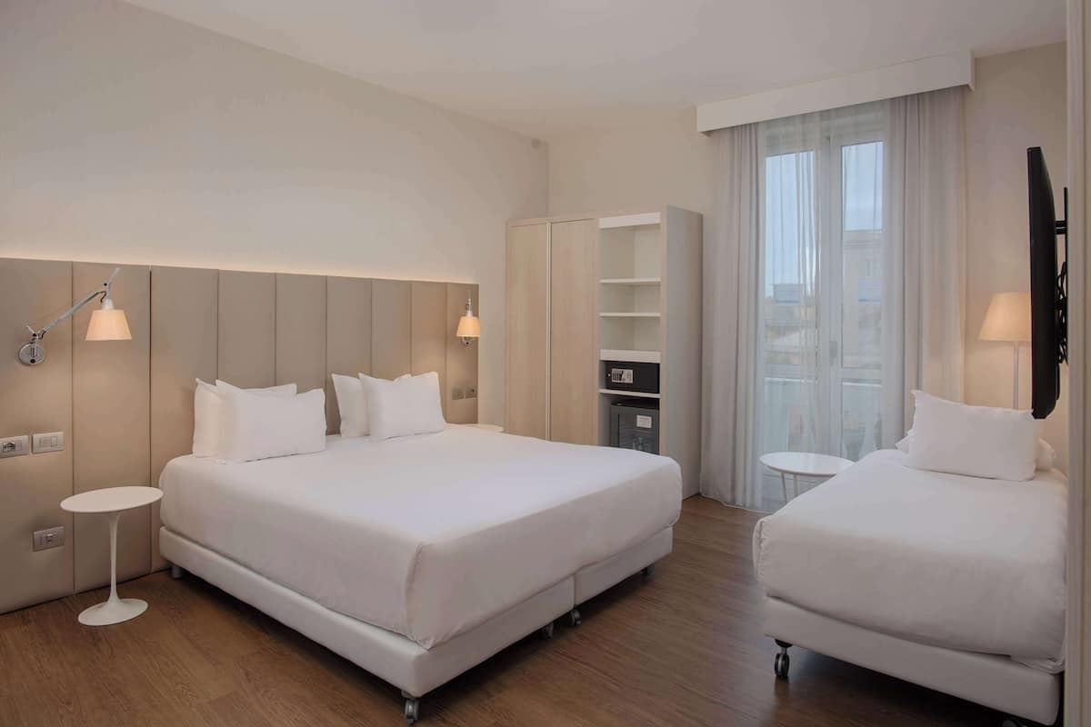 A hotel room with a large bed, a smaller bed, a desk, a wardrobe, and a TV.