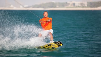 Une personne fait du wakeboard sur une étendue d’eau, avec un pont en arrière-plan.