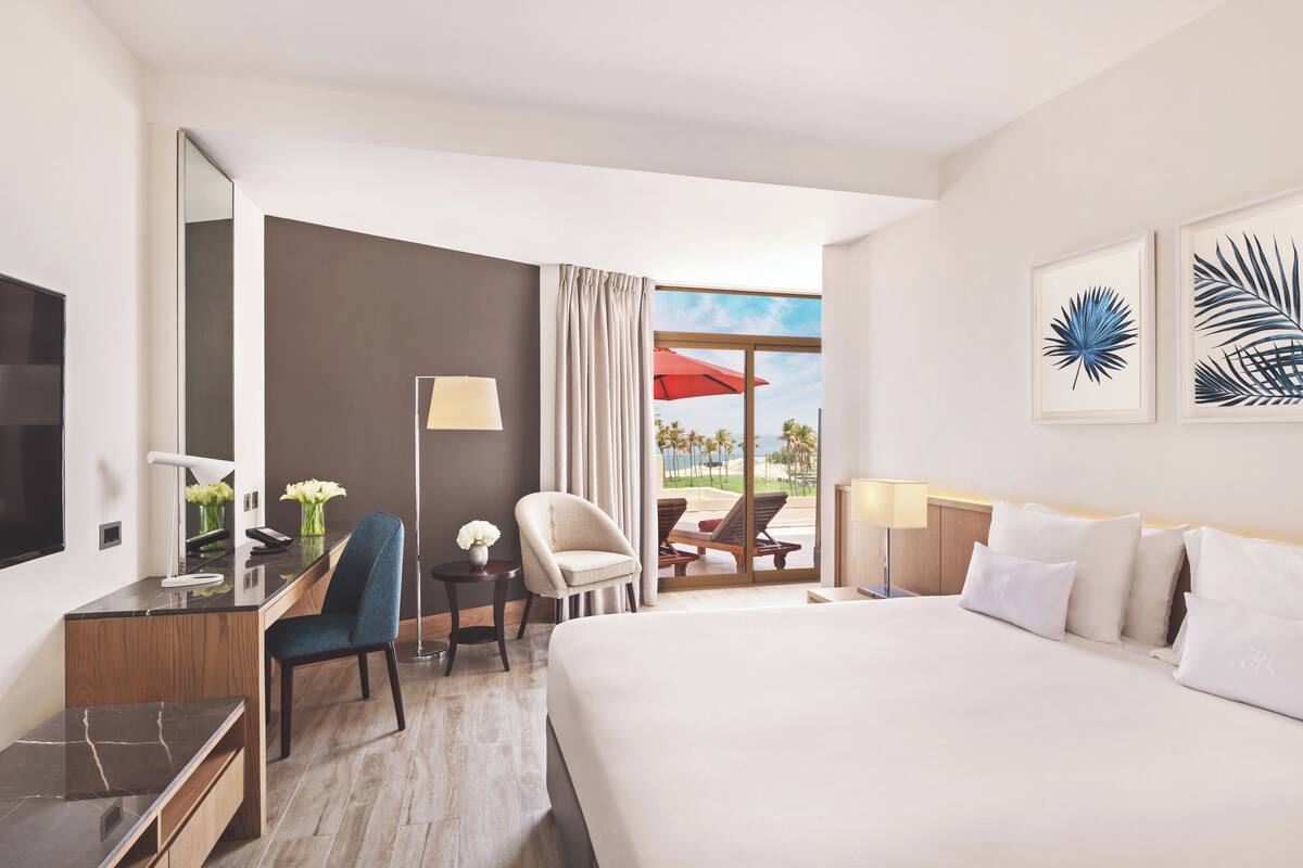 A hotel room with a bed, desk, chair, and a view of the outdoors.