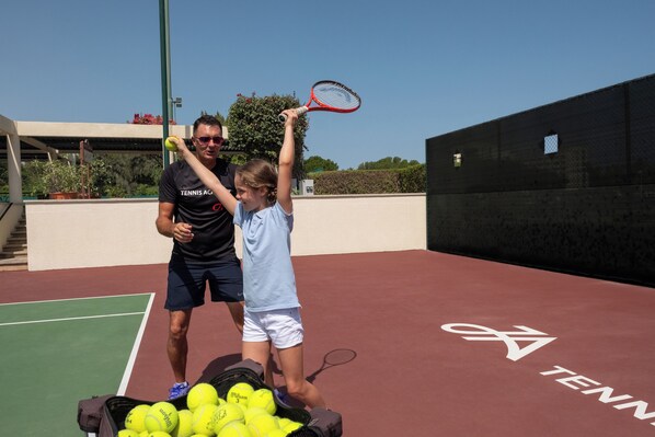 Una cancha de tenis con una red, una bolsa de pelotas de tenis y una raqueta.