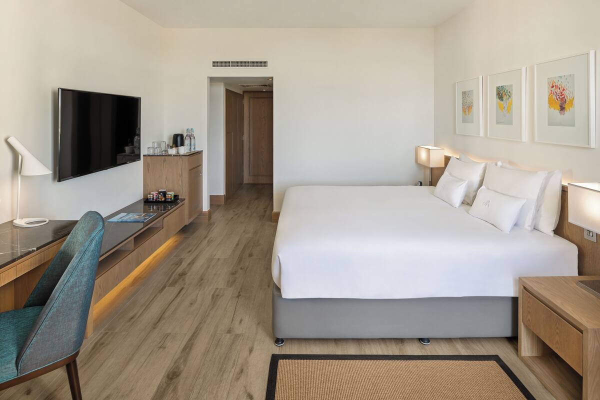A hotel room with a bed, a desk with a chair, a TV, and artwork on the wall.
