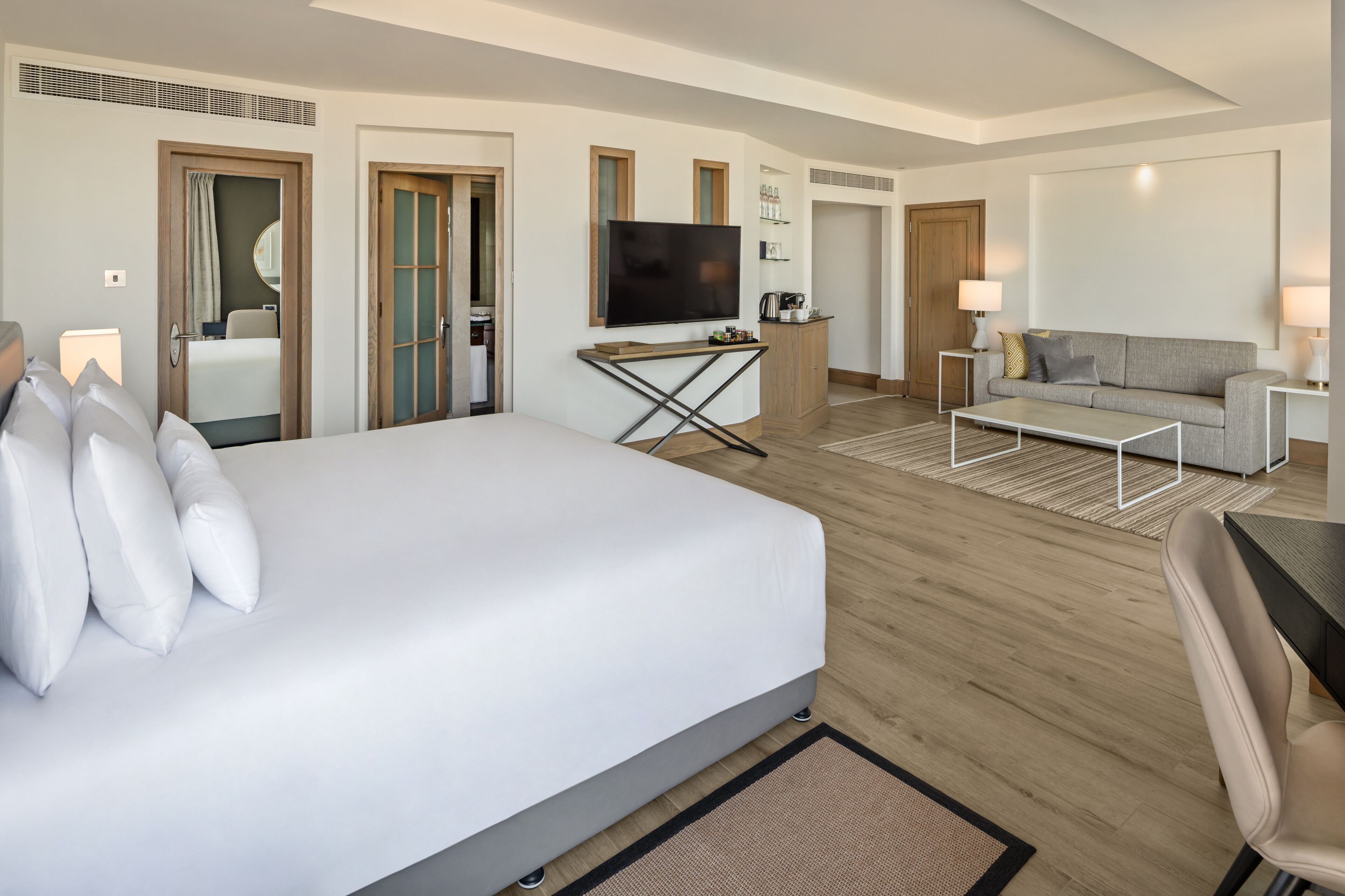 A modern hotel room with a large bed, a flat-screen TV, a sofa, and a coffee table.