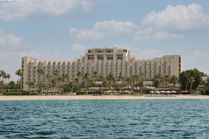 Un hotel grande con varios pisos, ubicación frente a la playa y un área de piscina con sombrillas.