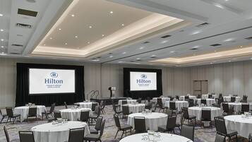 A conference room with multiple round tables, chairs, and a large screen displaying the Hilton logo.