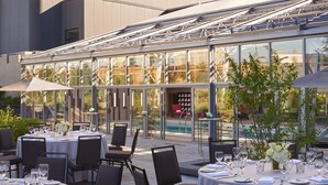 Ein Außenbereich zum Essen mit runden Tischen, Stühlen und Sonnenschirmen mit Blick auf einen Pool und Grünflächen.